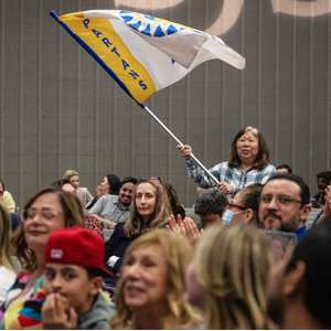 A staff member stands up in the crowd waving an SJSU flag showing pride.