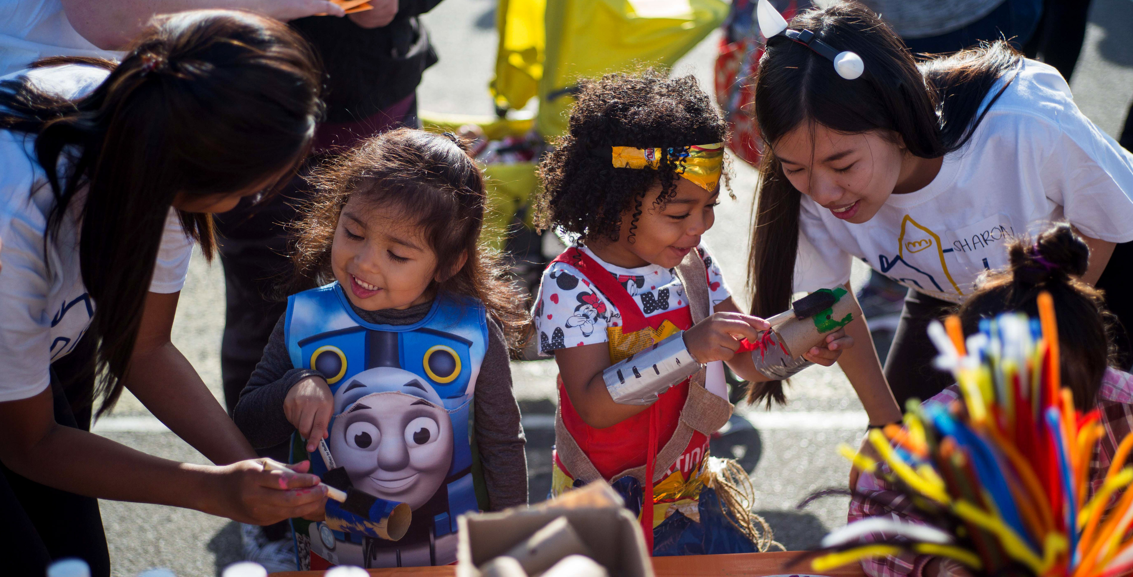 Student volunteers help two kids with arts and crafts during a halloween event.