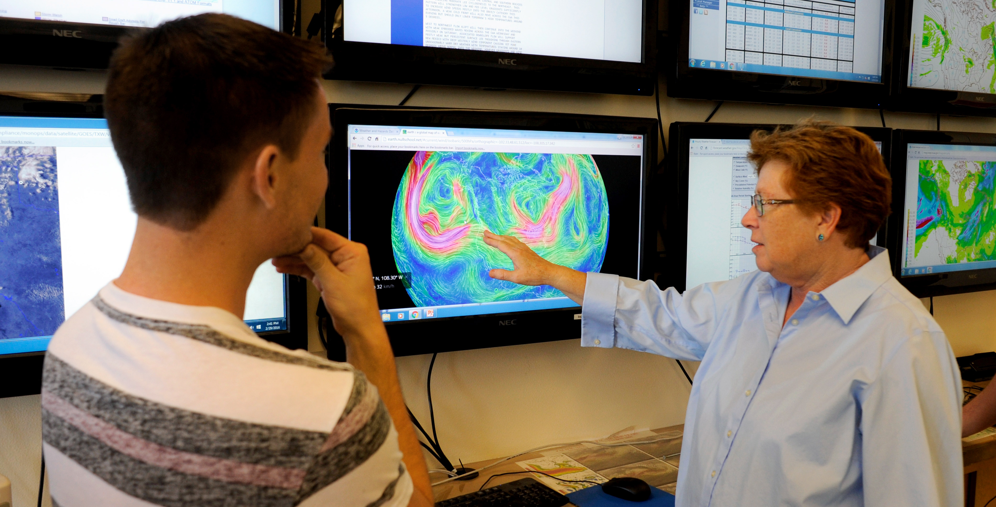 A professor points at the monitor showing weather patterns to a student.
