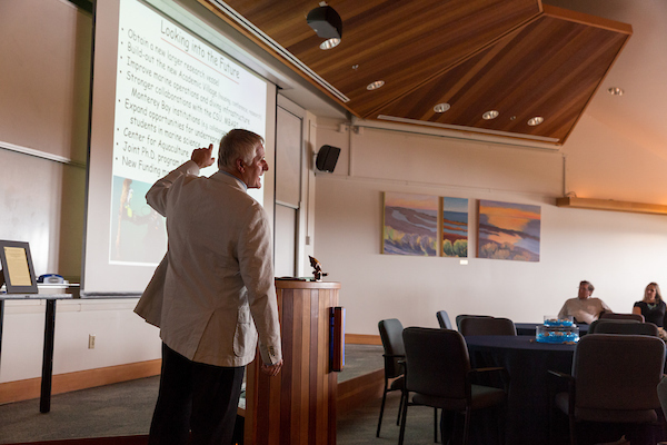 Professor in classroom pointing up at information of the projector screen,