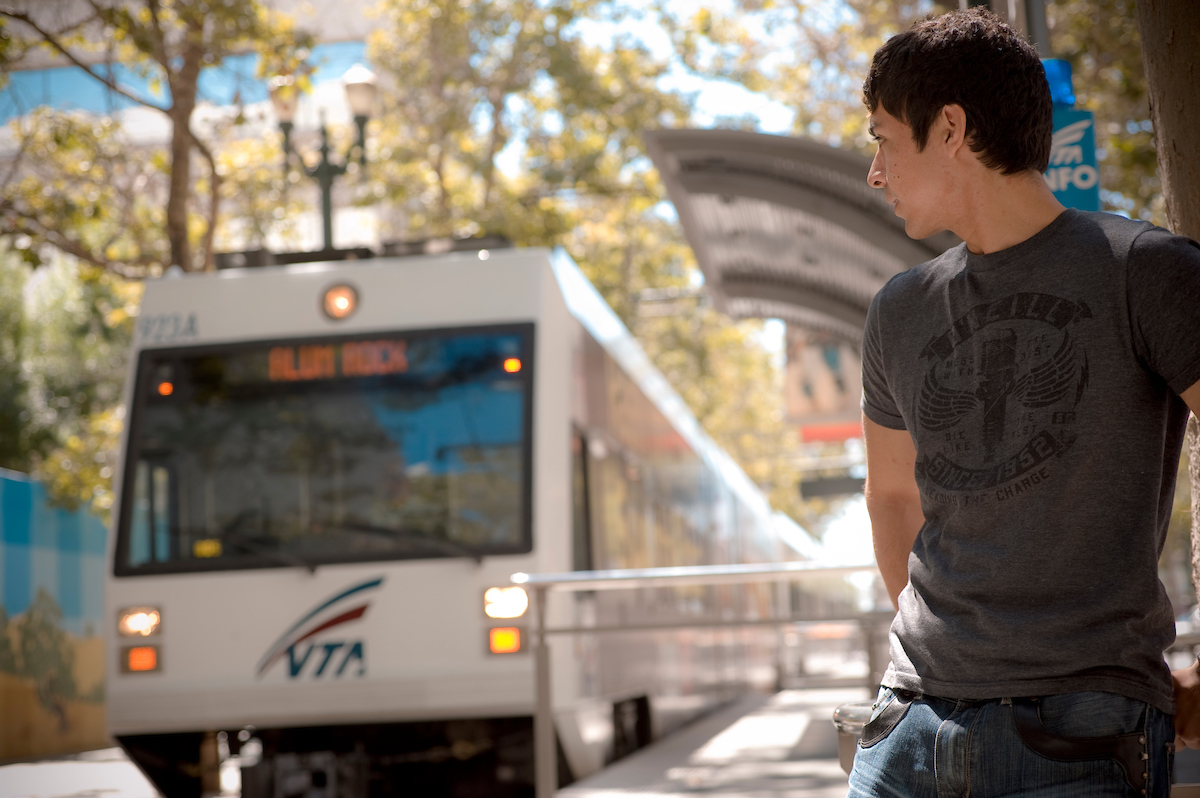 A student looking back at the approaching VTA light rail on a sunny day.