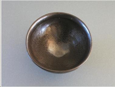 The interior of an "oil spot" temmoku bowl. The glaze is brown but there are small iridescent patches like oil floating on the water. This happens because the glaze is super-saturated with iron and it crystallizes under certain circumstances in firing.