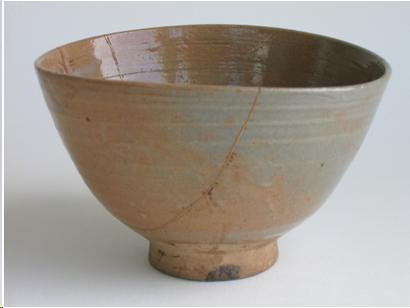 A grey and pink glazed Korean tea bowl. The cracks are mended with gold lacquer. It is the shape of a rice bowl. 