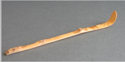 A bamboo tea scoop. It is a little shorter than a pencil and about as wide. The tip is curved upwards. This end is used to scoop the tea. The surface of the scoop is still covered with the speckled skin of the bamboo. This scoop has three natural bamboo nodes in it. It has a strong, rustic feel to it. 