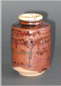 A cylindrical thick tea container with a mouth about an inch wide at the top. An ivory lid seals the mouth of the jar. Buff-colored, unglazed clay can be seen at the bottom of the jar. The glaze is brown with darker drips of the thicker glaze running down from the jar's shoulders.