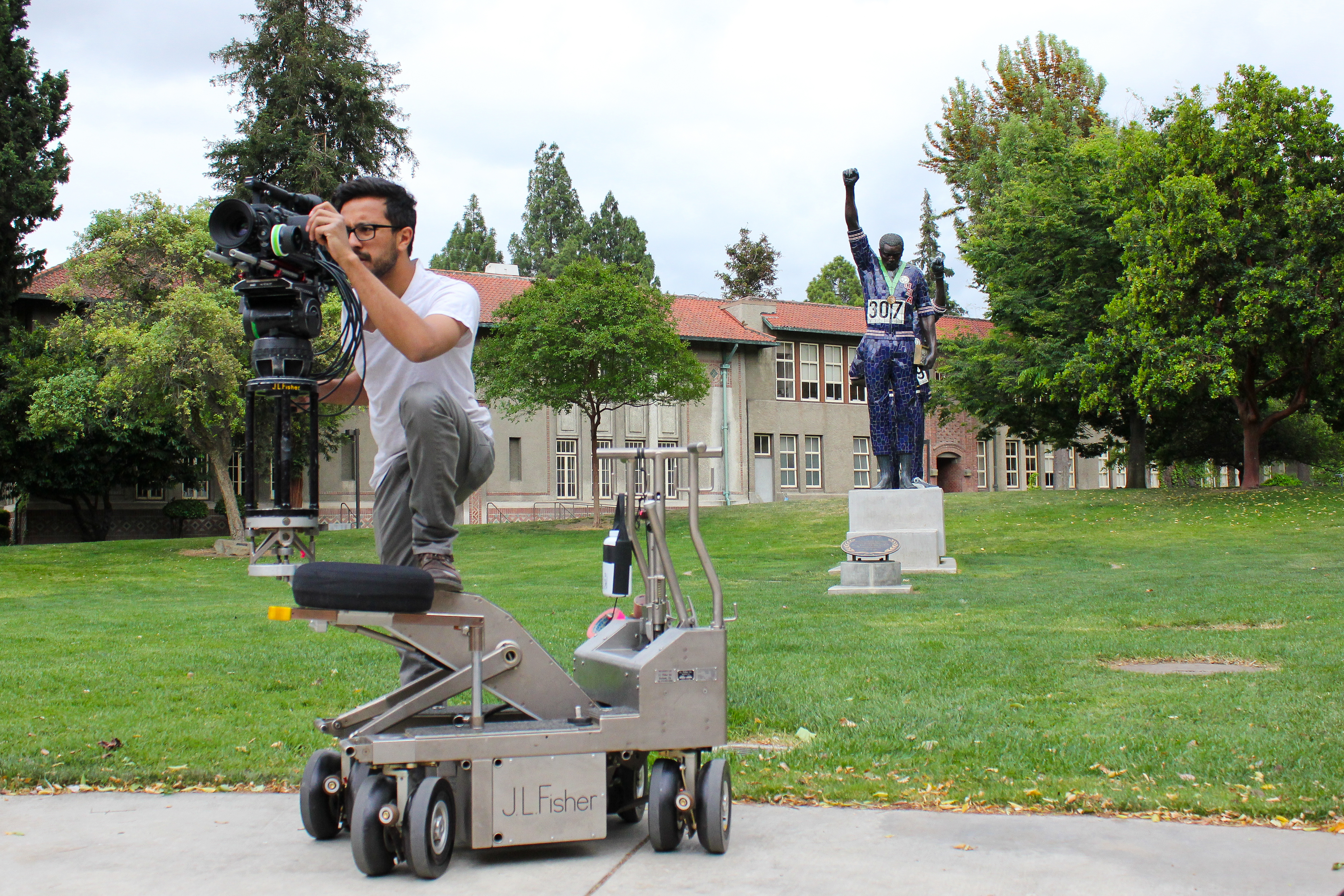 A student stands on a dolly with a camera while filming for a project.