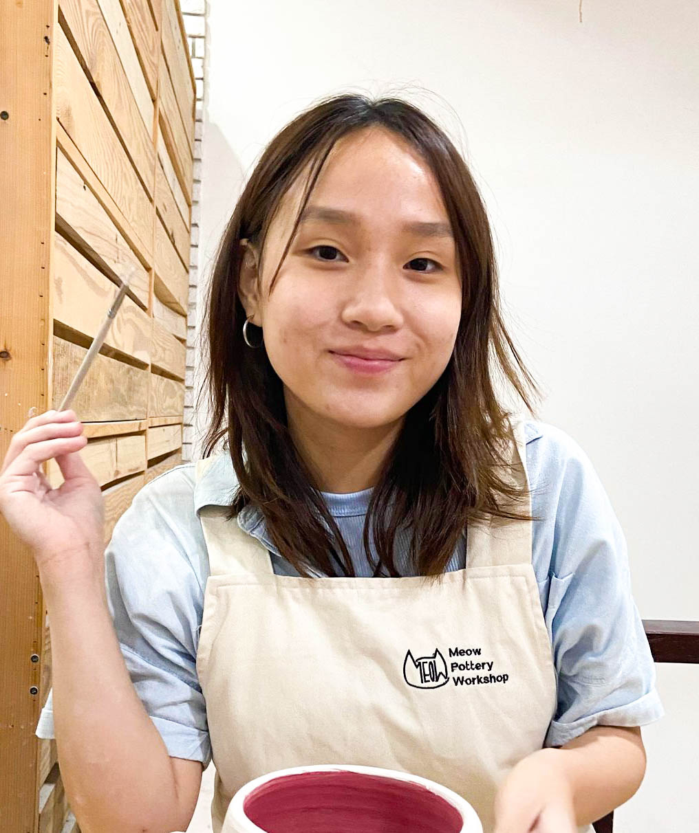 smiling person in apron with paintbrush and pottery