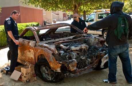 Police officer and two students look at a car total in traffic accident
