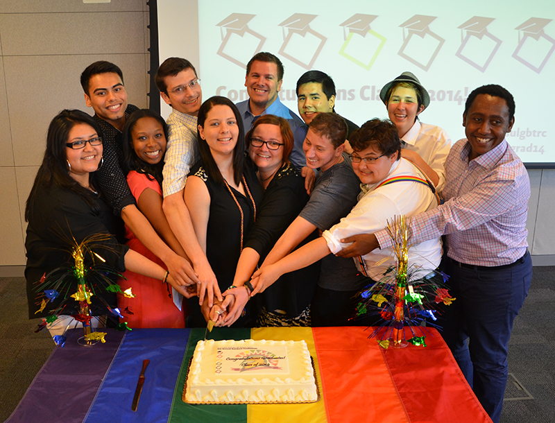 Rainbow graduates cutting a cake together.
