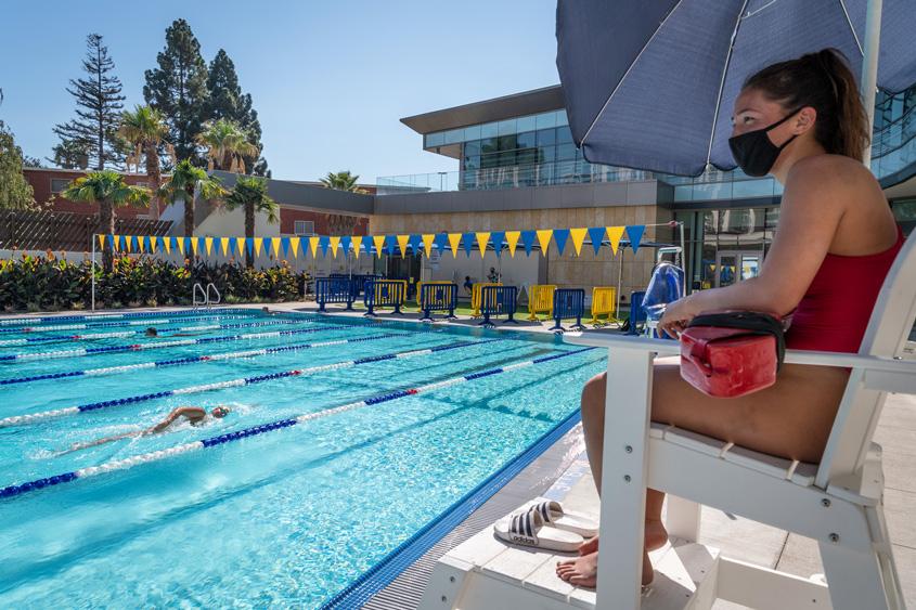 A student lifeguard sits on duty watching other students swim.