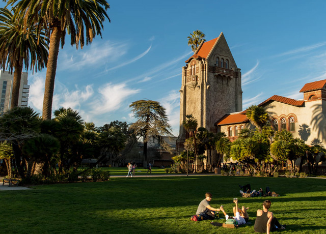 students relax on the grass in front of Tower Hall on a sunny day.