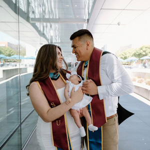 Fernanda Renteria-Gonzalez and David Salinas wearing their grad stoles and holding their newborn baby.