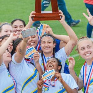 Aimee Ramos smiling while holding up a trophy with her teammates.
