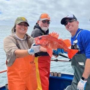Researchers on a boat holding a bright orange fish.