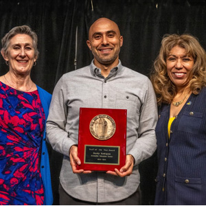Randy Rodriguez holding a staff of the year award in his hands with the president beside him.