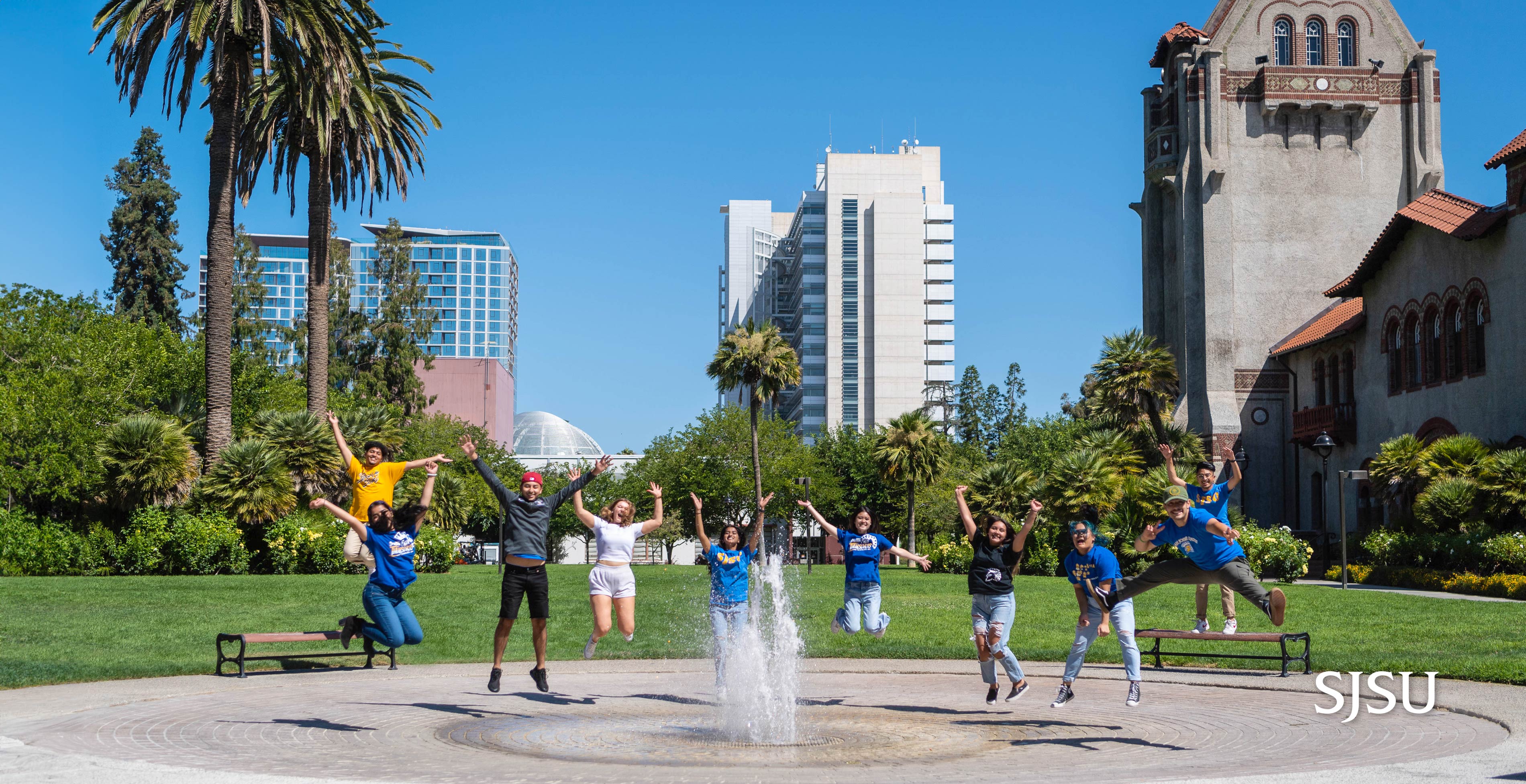 SJSU students jumping up in mid air in different poses in front of the fountain next to Tower Hall on campus.