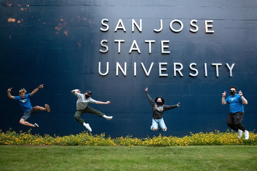Students jumping up in the air in front of the SJSU sign.