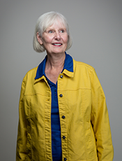 waist-up photo of Diana Hunter, caucasian female with short white hair, wearing a yellow collared jacket lined with blue