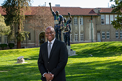 Black male in suit in front of Victory statue at SJSU