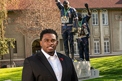 Black male in suit in front of Victory statue on San Jose States campus