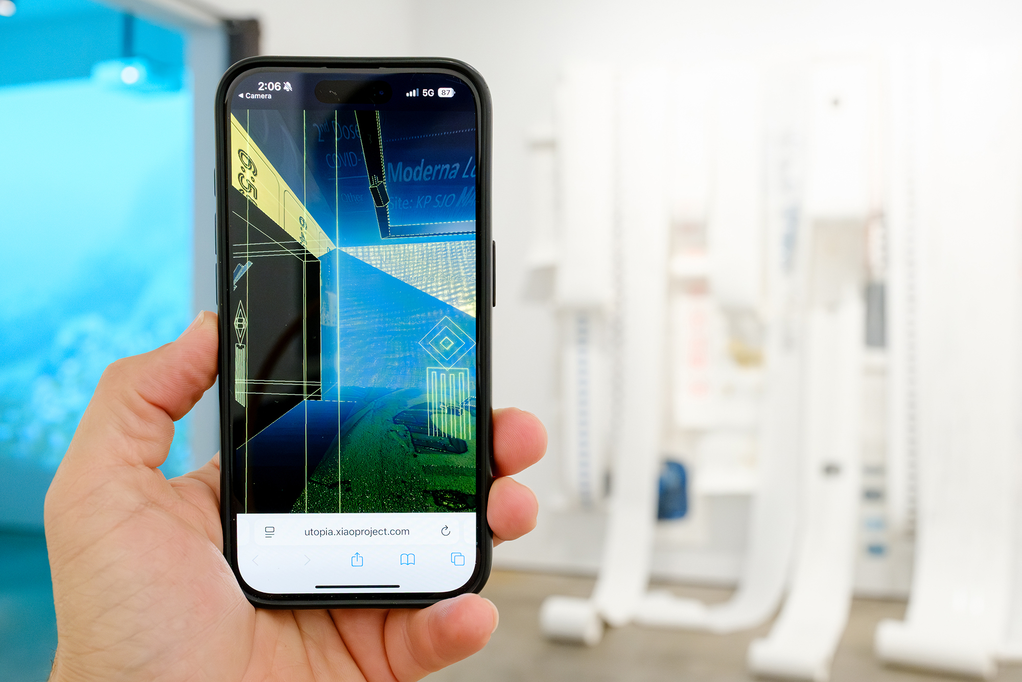  Individual holding a smartphone that features an Augmented Reality art installation inside a gallery.
