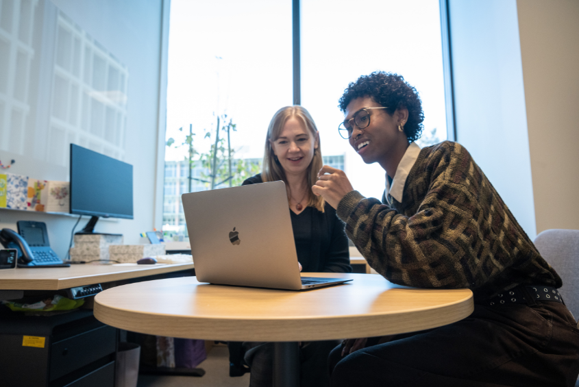 Student meeting with an employee, looking at a laptop computer together.
