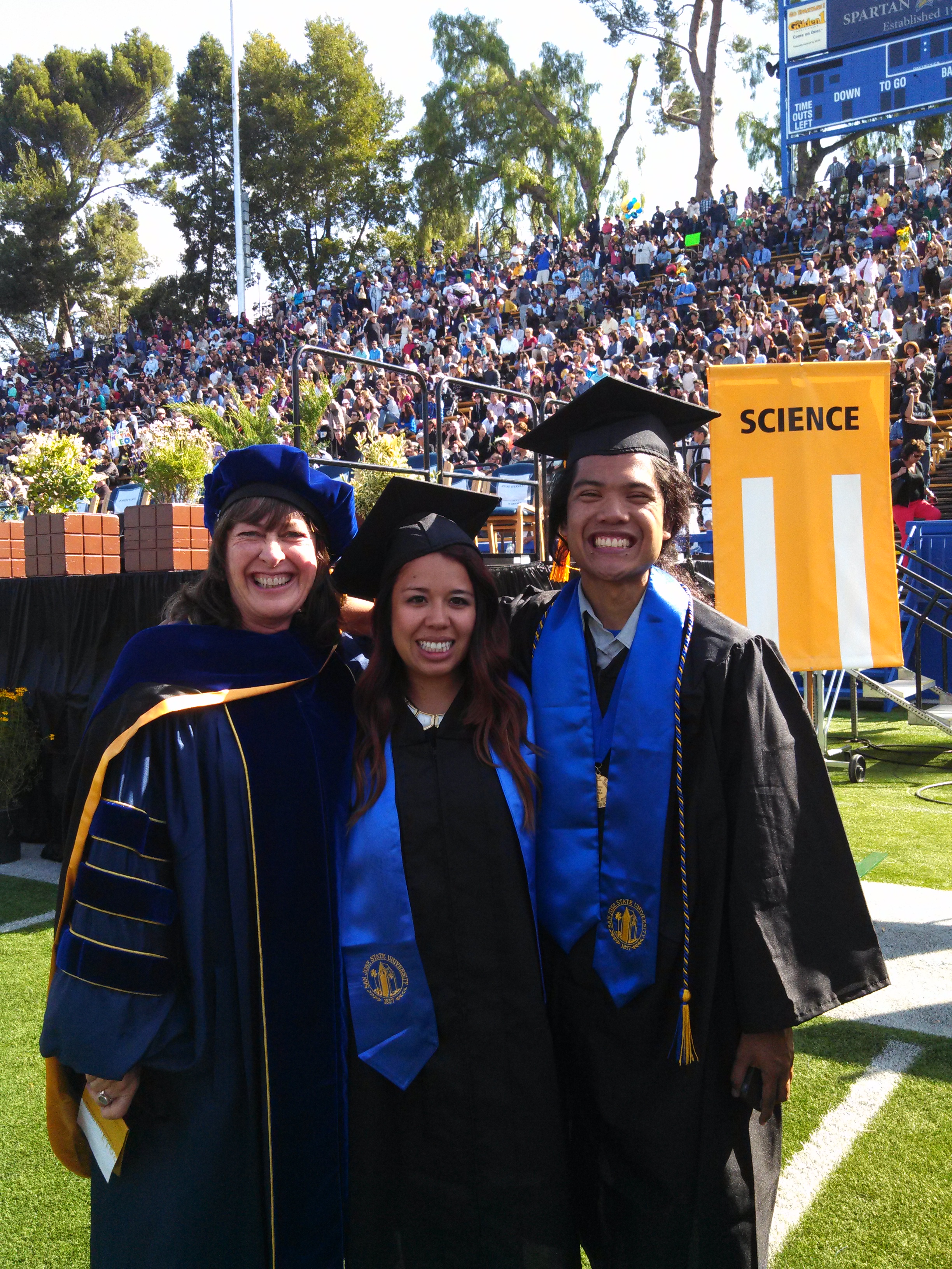 A professor posing with two MARC students at graduation in their caps and gowns.