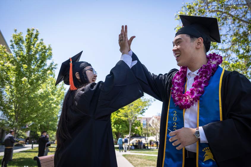 Two graduates high-five after the ceremony.