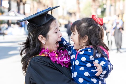 Graduate in Regalia with their child in arms looking at each other with faces of joy.