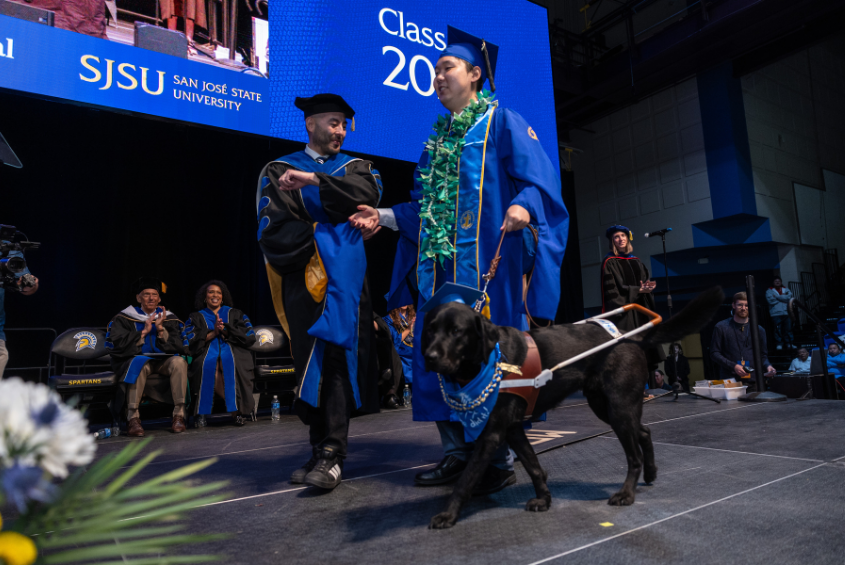 Student with a guide dog crossing the stage