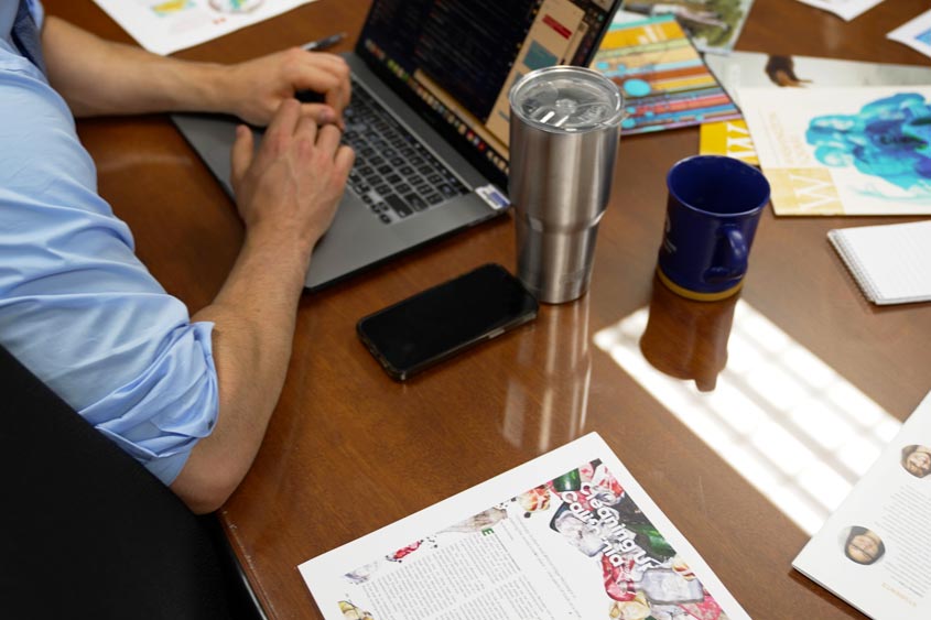 A man on a computer typing with branding materials on their desk.