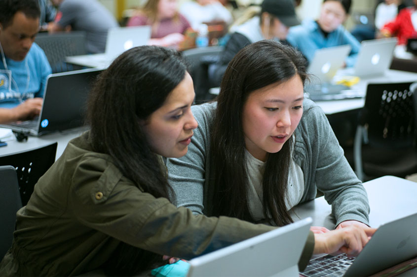Two students talking and both pointing to a computer screen.