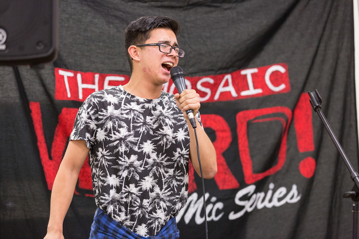 Student performing in front of a backdrop that says, MOSAIC's Word Poetry Series.