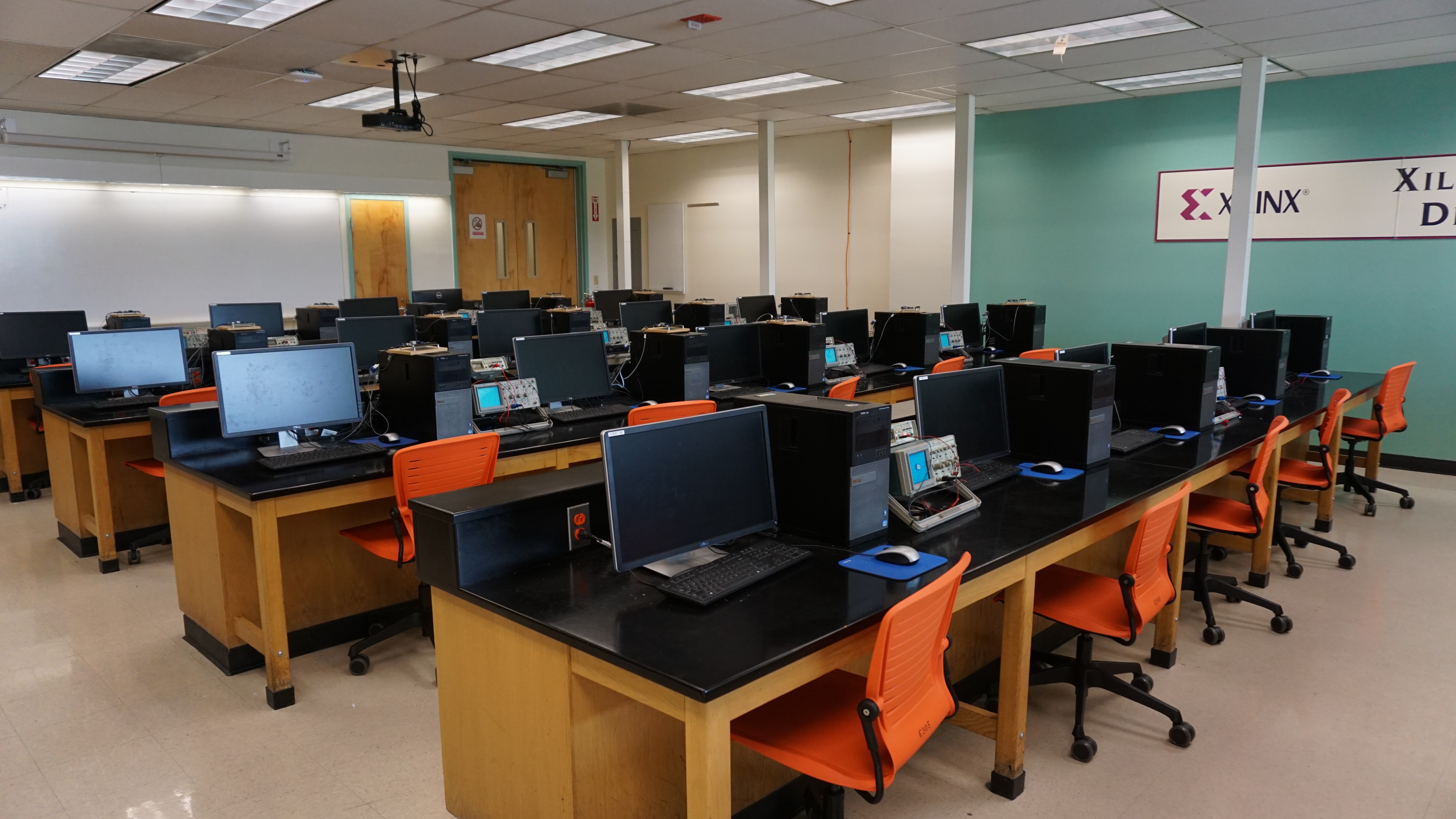 A classroom with computers, orange chairs, and a bright teal wall with the Xilinx logo.