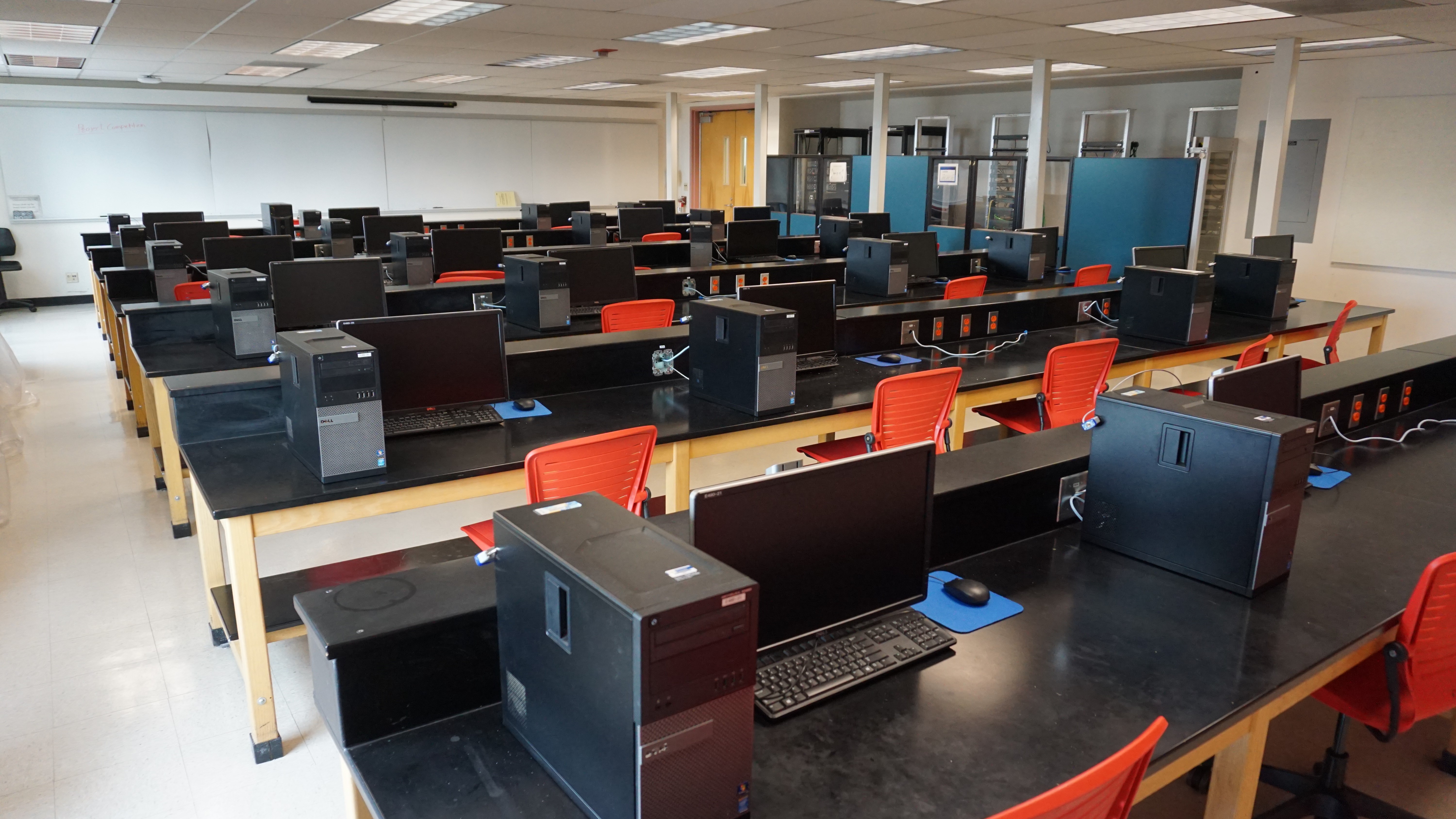 A classroom full of computer stations and bright orange desk chairs.
