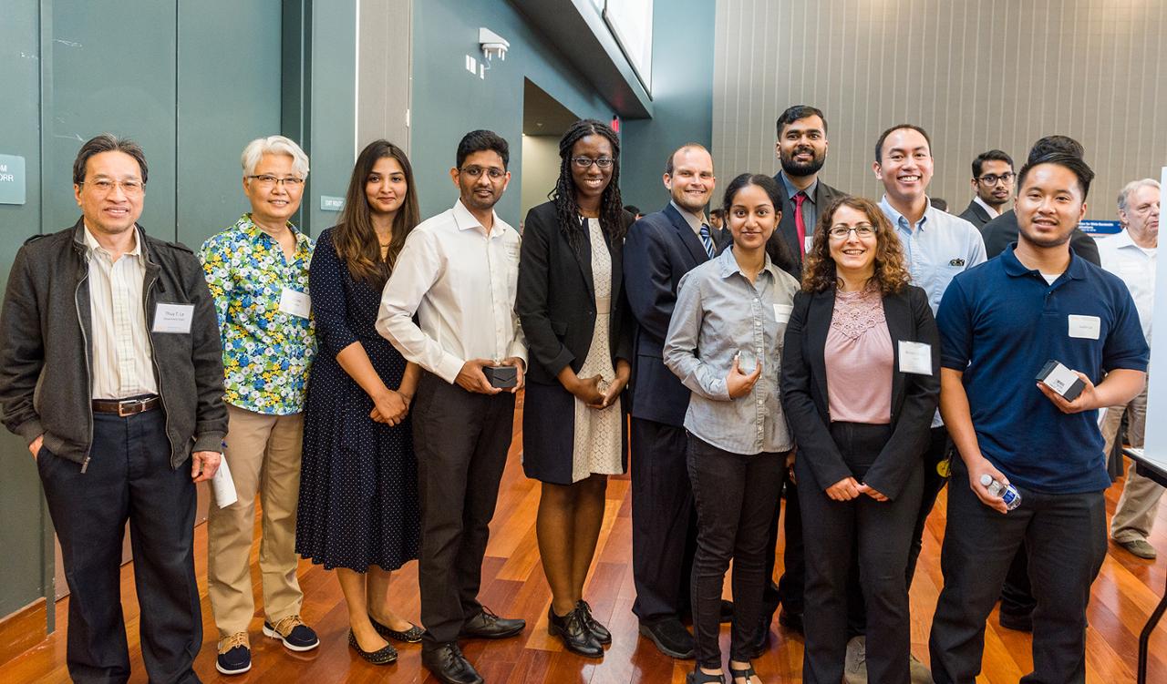 A formally dressed group of students and faculty stand together and smiling.