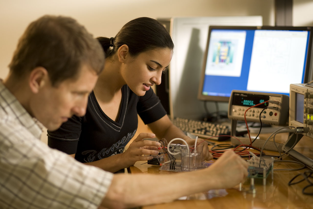 Two students sit together at a desk as they work with electronic components.
