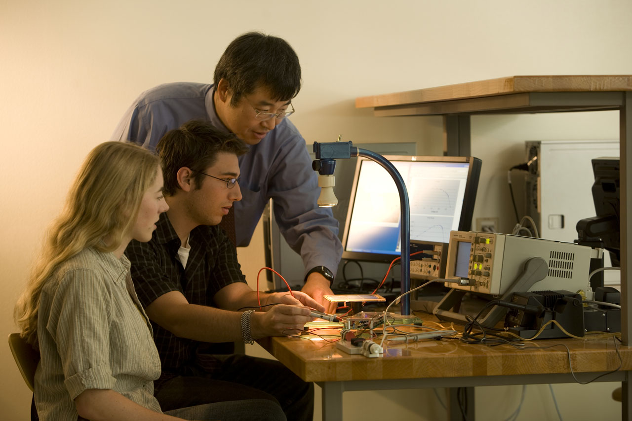 A professor is helping two students with their electrical engineering project.