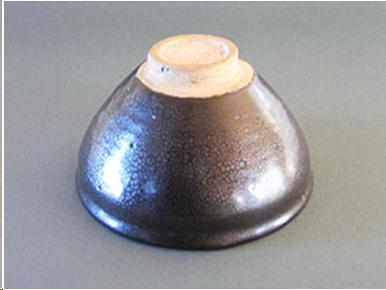An "oil spot" temmoku tea bowl shown from the bottom. The foot is small, shallow, and unglazed. The clay is buff-colored.