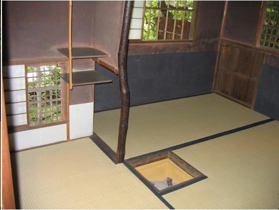 A two a three quarter mat tea room. A small hearth with a wooden frame is cut in the floor. The area where tea is made is divided from the area where the guest will sit by a 1/2 wall which is plastered on the top but open at the bottom. The edge of the wall near the hearth is formed by a an irregular tree branch. In the area where tea is made, there a small window open to the garden. It may be covered by sliding shoji, wood window frames covered with white Japanese paper. The guests' side of the room has two windows open to the garden and a small wooden door about three feet square. The guests's side of the room is covered with blue paper to a height of about 25 inches.