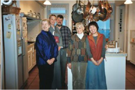 A group of tea students stands with their teacher in the kitchen. There is one man, two Caucasian women, and one Japanese woman. They have been preparing the food for a tea gathering.