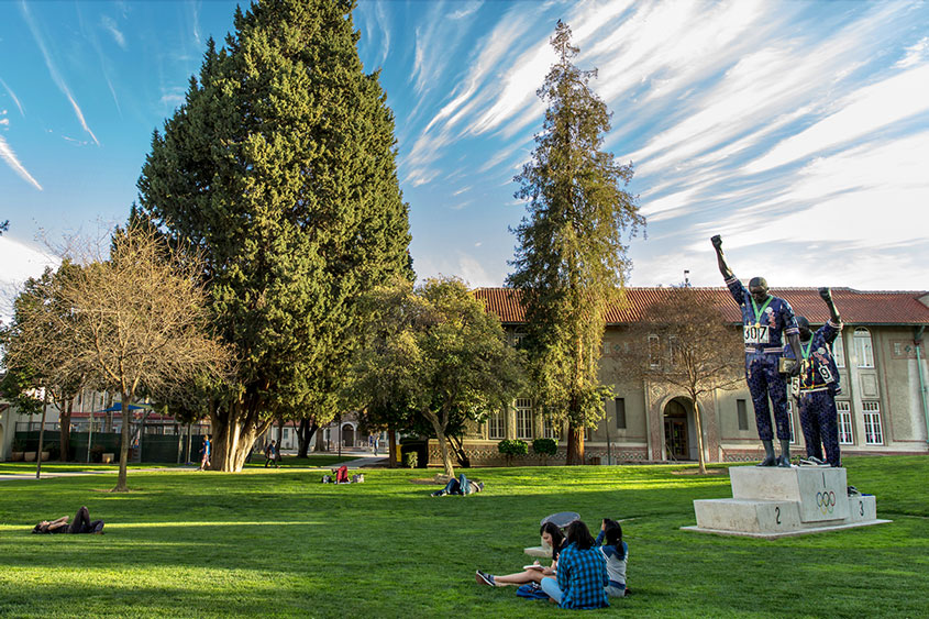 Students relaxing on the lawn next to the Tommie Smith and John Carlos statue.
