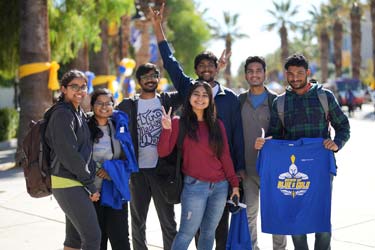 A group of international students stands outside on the campus of SJSU holding Spartan gear.