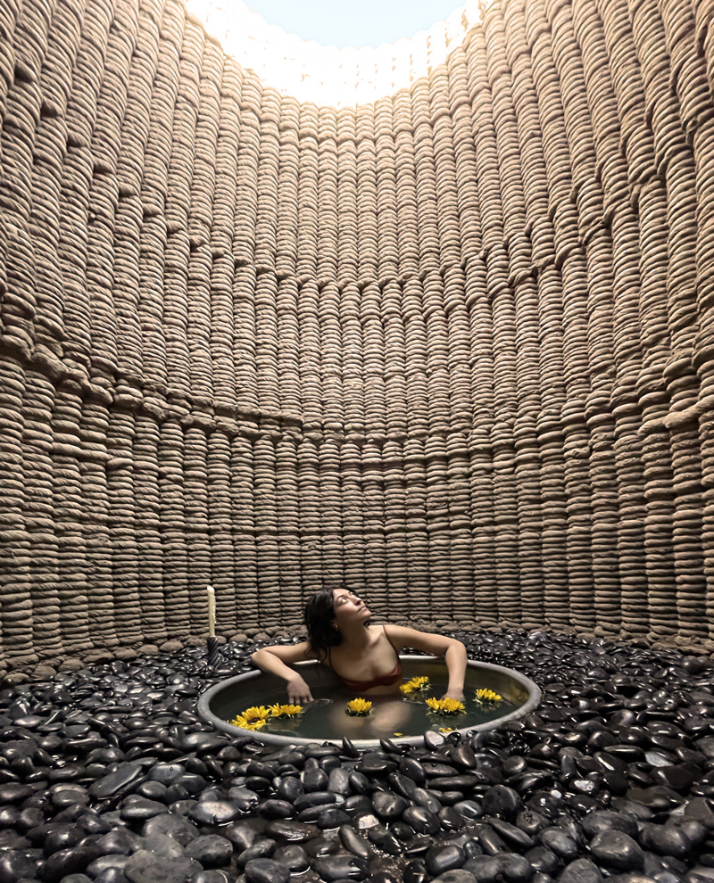 A woman sits in a bath inside a 3D printed Casa Covida.