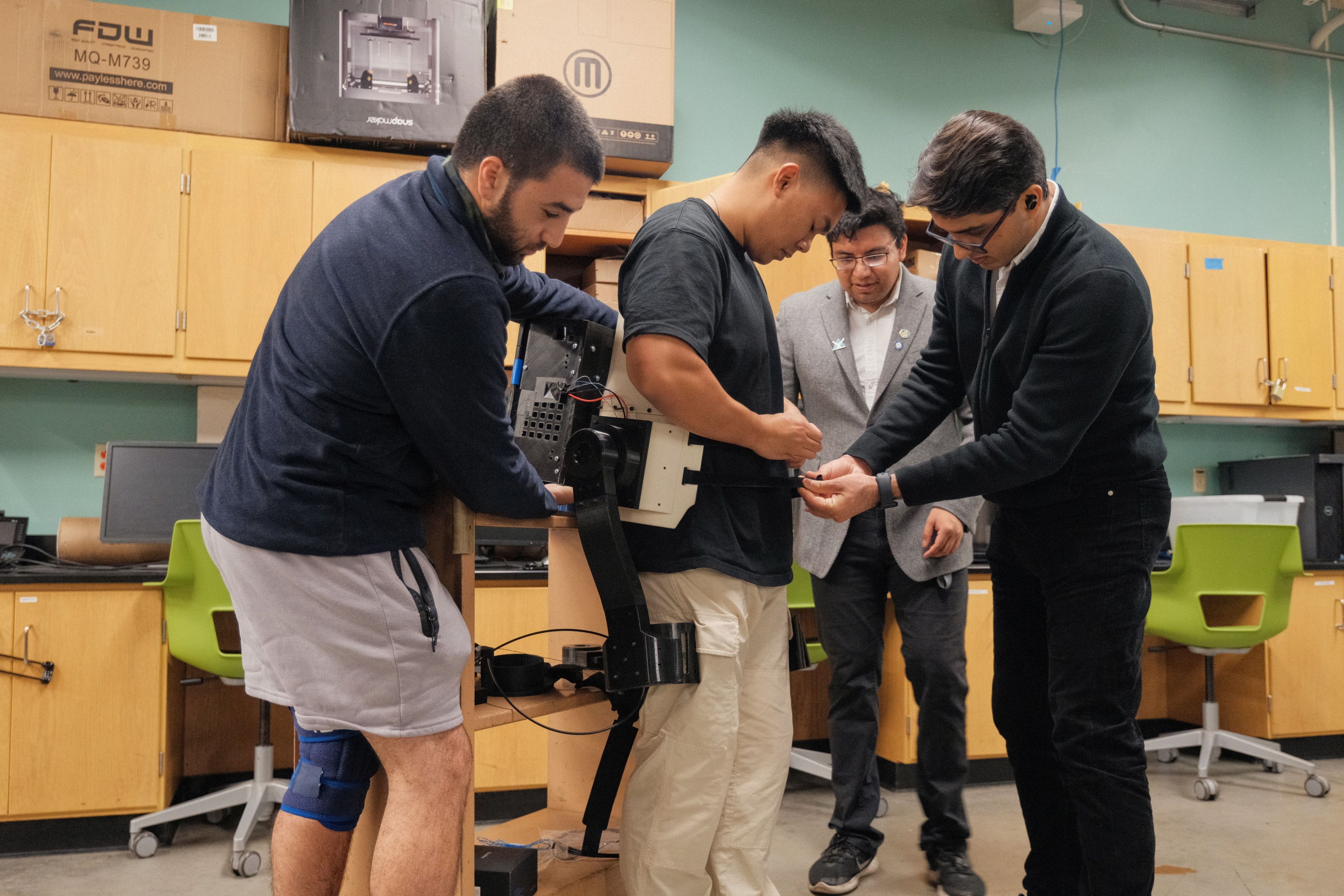 Professor Mojtaba Sharifi and student researchers at SJSU test the exoskeleton on a human wearer. student research, STEM, engineering, exoskeleton, innovation, patents