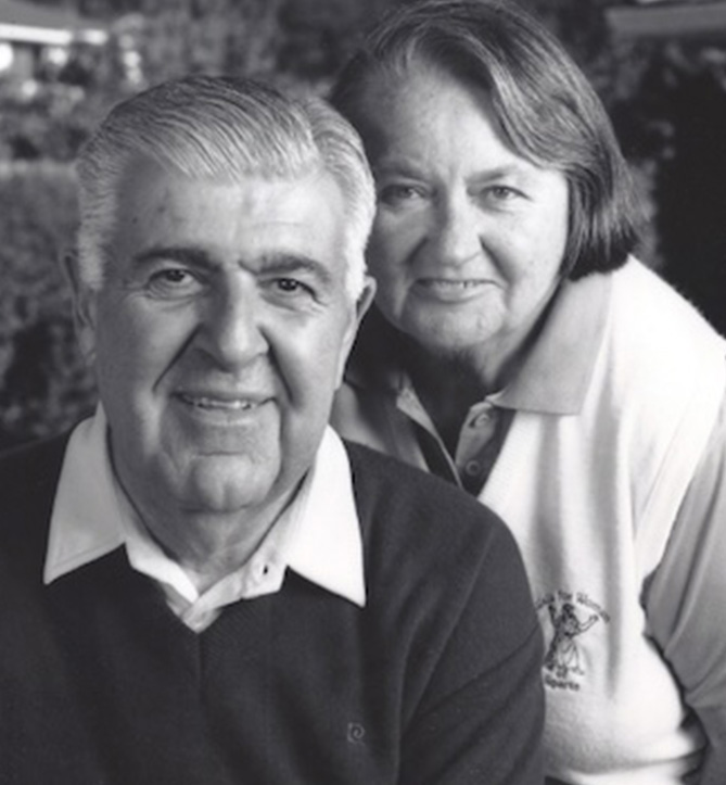 An older man in a dark sweater and a white collard shirt poses with an older woman in a white vest and collared shirt. Arm and Pat Hanzad, giving, philanthropy, scholarships