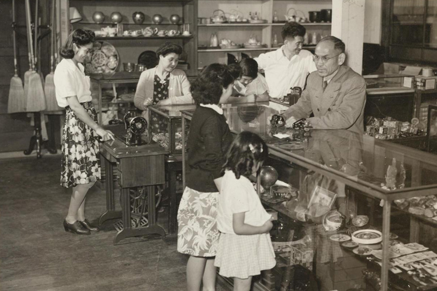 Kogura Gifts store, c. 1940s, courtesy of Richard Kogura. Young women approach Kohei Kogura, store proprietor, at the counter. Japantown, San Jose, Japanese American, black and white