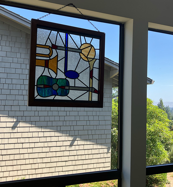 stained glass window with images of instruments hangs from a window. Charlene Archibeque, music, choir, professor emerita