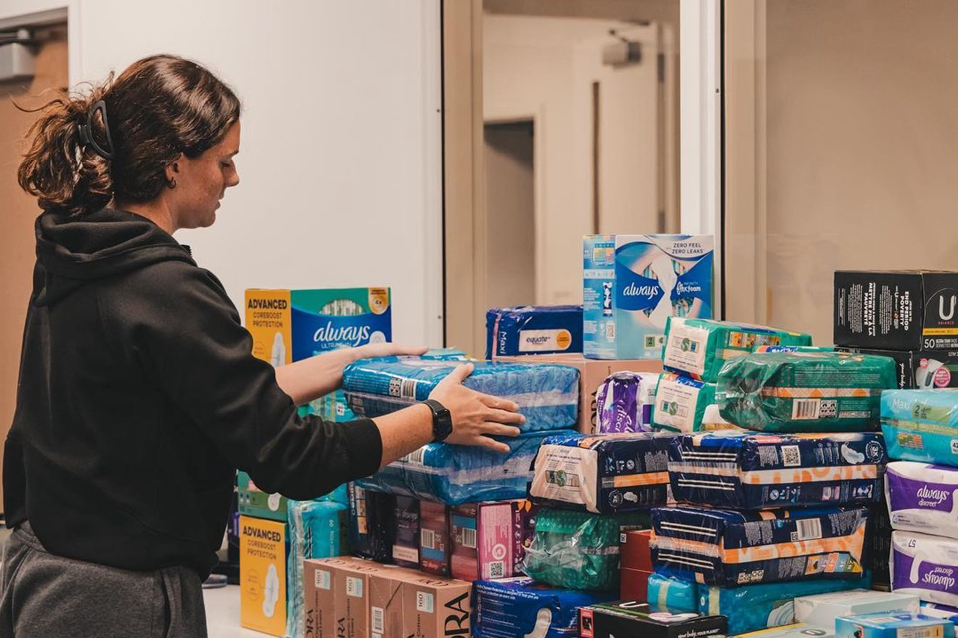 A female SJSU student-athlete organizes piles of sanitary products for community service drive. SJSU athletics, student athlete, community service, Spartans, Beyond Sparta