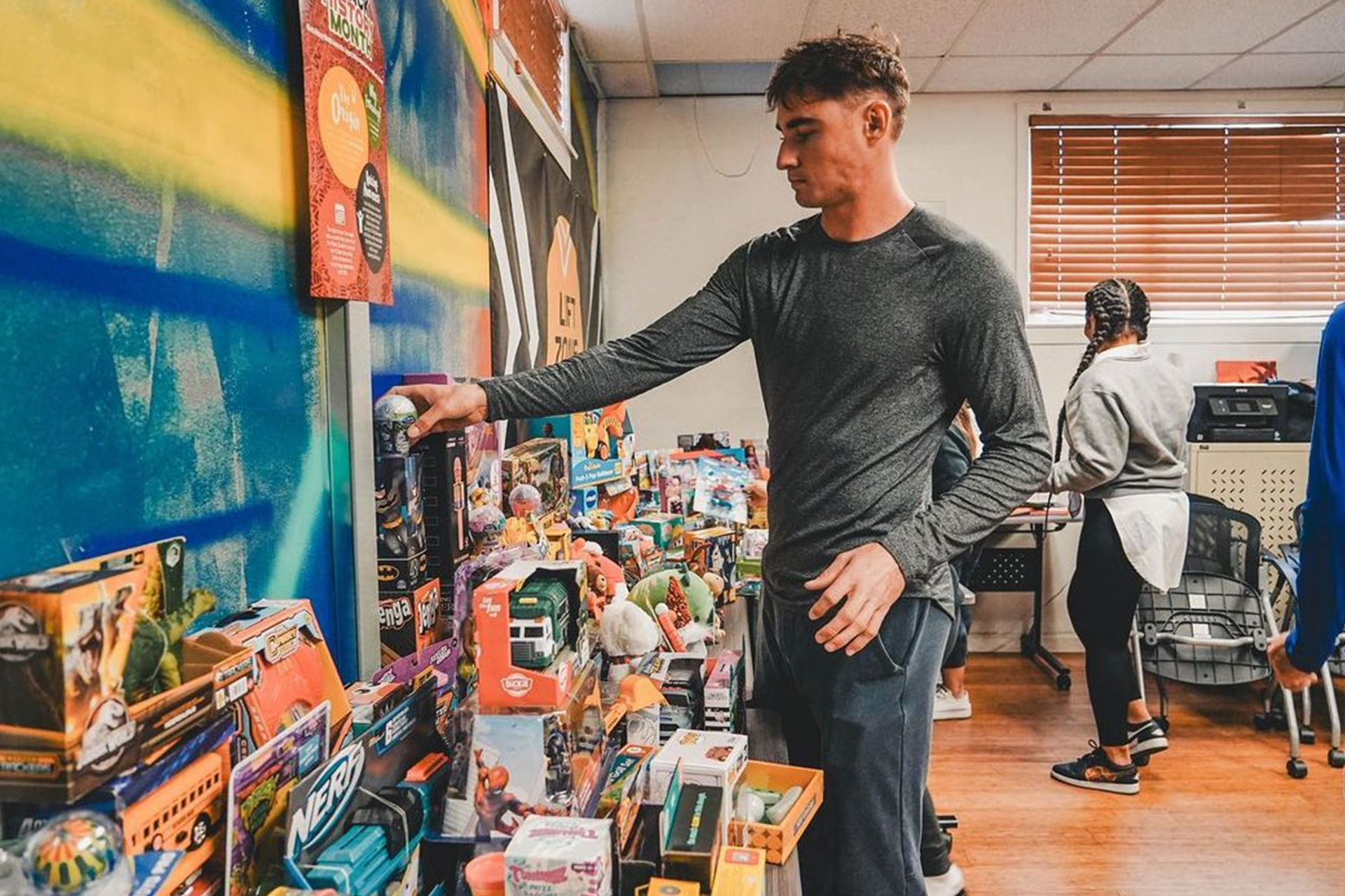 A male SJSU student-athlete helps organize and place toys on a pile for a charity toy drive. SJSU athletics, student athlete, community service, Spartans, Beyond Sparta, toy drive